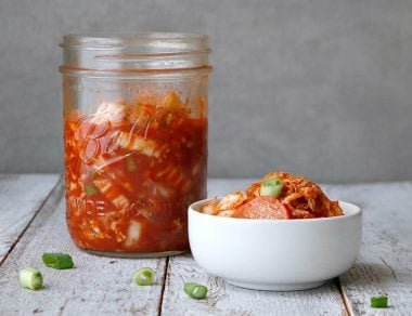 Shredded cabbage ferments with radishes, scallions, and ginger for a homemade, Paleo-friendly kimchi rich in gut-healing probiotics.